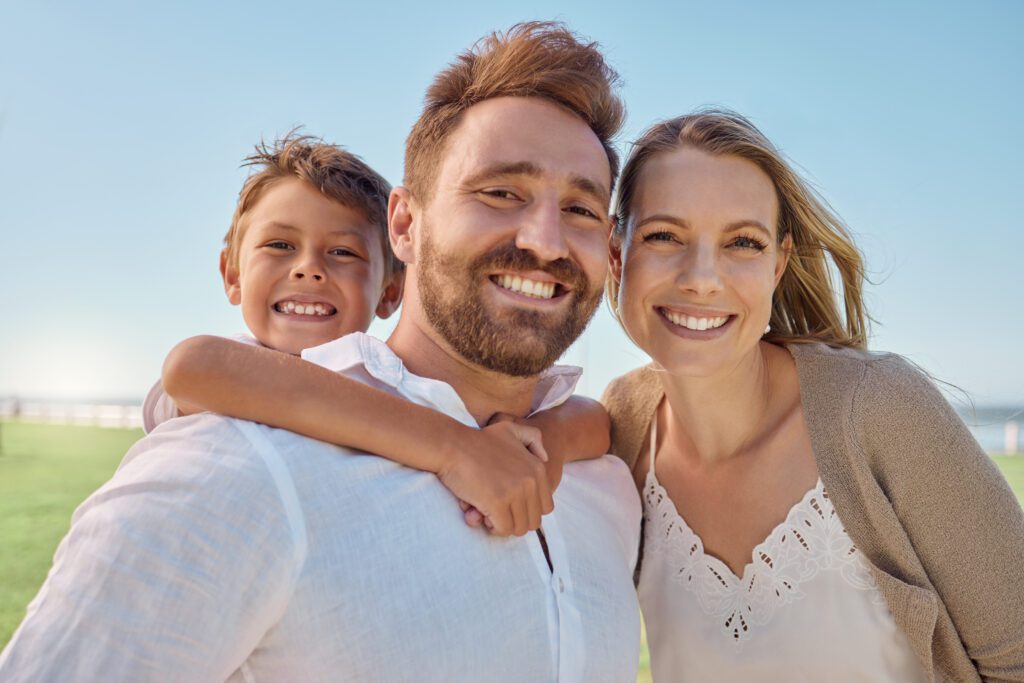 Family, Children And Piggyback With A Man, Woman And Son Outdoor On A Field During A Vacation Or Holiday Together. Kids, Travel And Love With A Mother And Father Bonding With Their Boy Child Outside