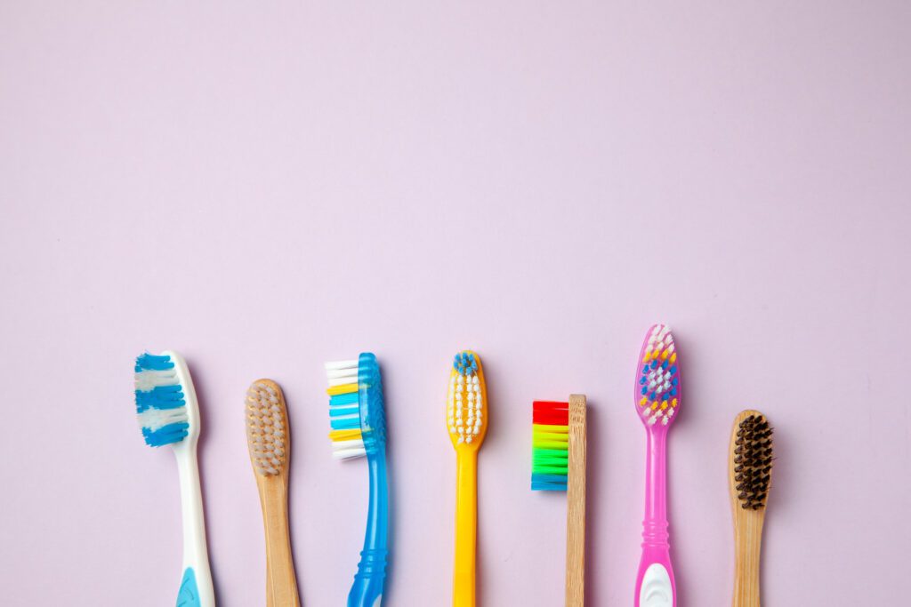 Many Colored Toothbrushes On Purple Background. How To Choose To