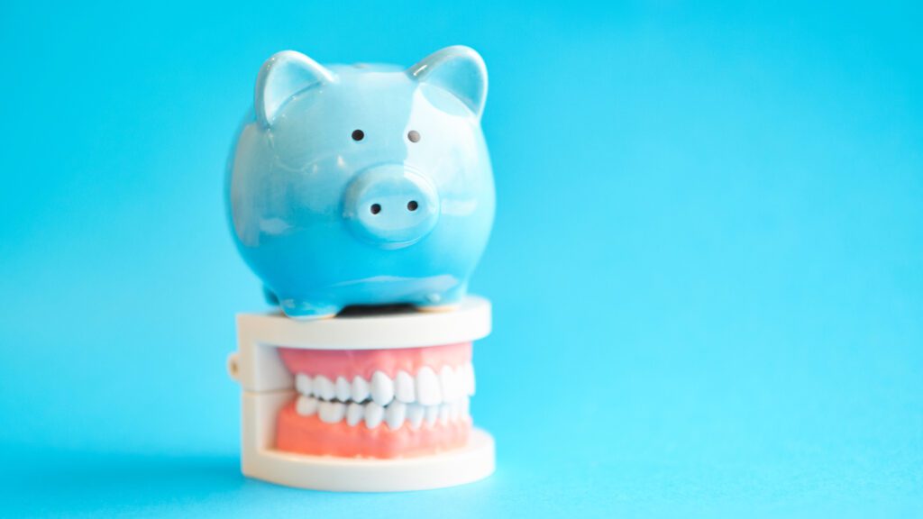 Piggy Bank With White Teeth Model On Blue Background. Tax Offset Concept. Medical Expense Deductions And Tax Breaks. Affordable Care Act. High Cost Health Care. Dental Expenses